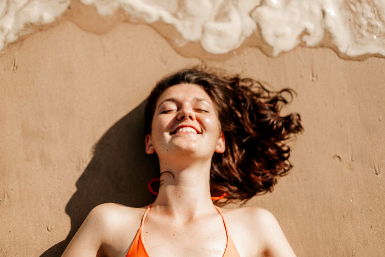 A smiling woman relaxes on Weligama beach, Sri Lanka, with waves gently breaking near her.