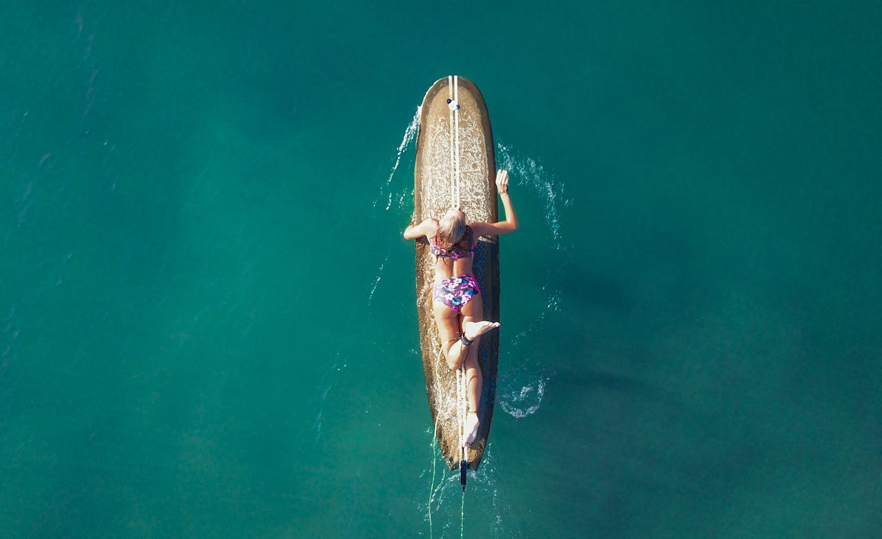 A woman relaxing on a surfboard in a calm turquoise sea, viewed from above, capturing the essence of a peaceful summer day.